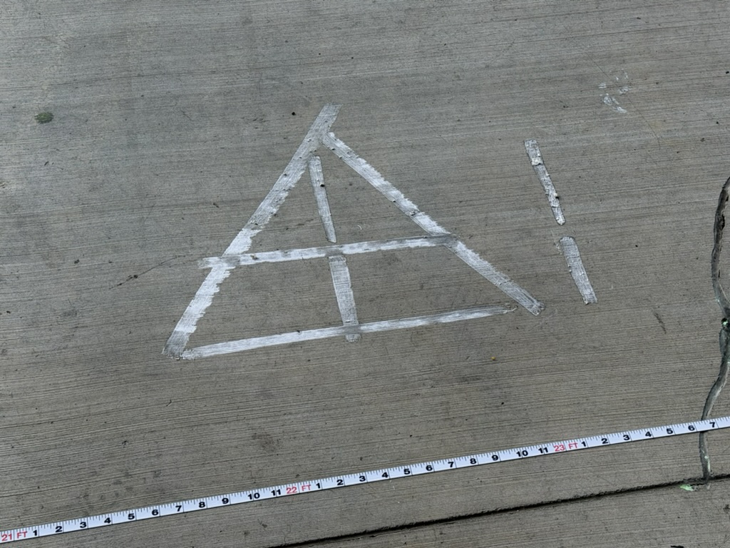 A rigging point marked out on the deck in tape and chalk, measured against a tape measure